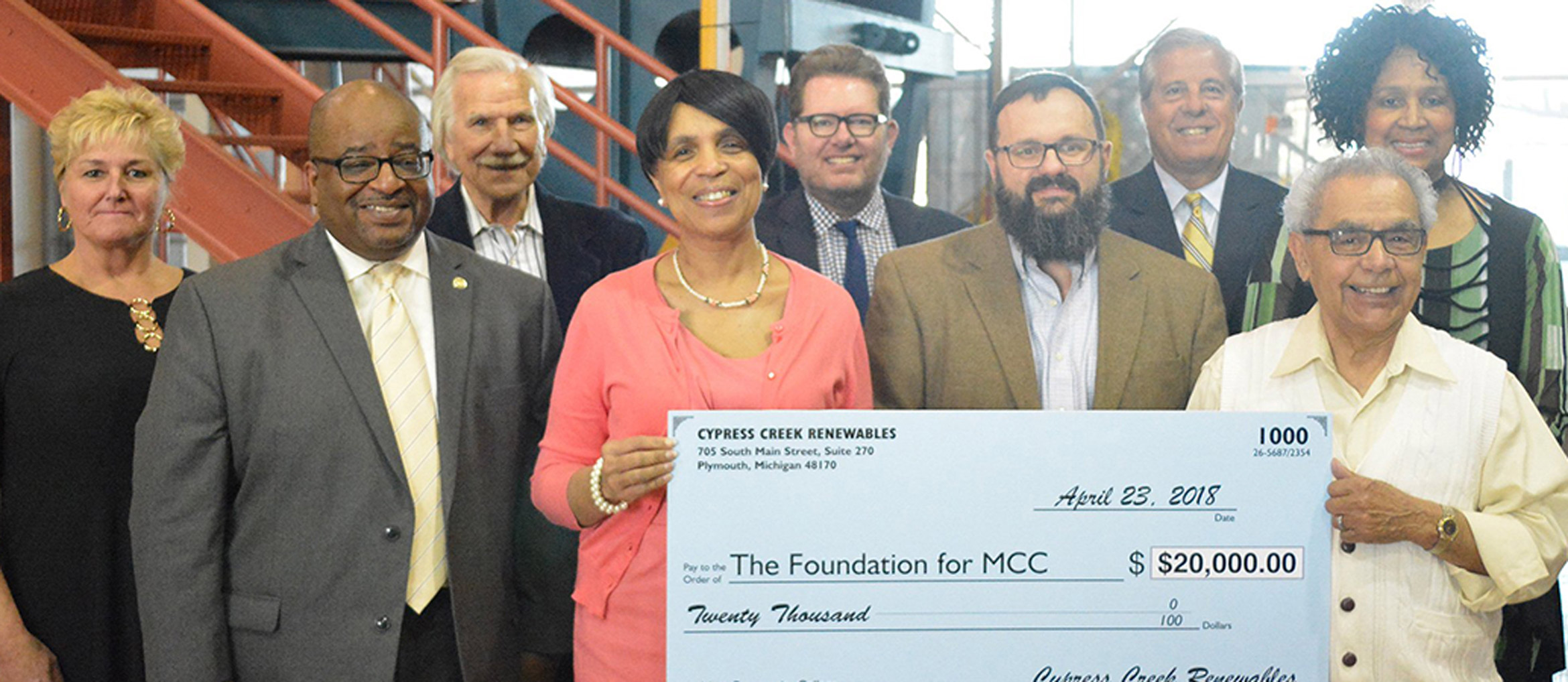 Group of men and women pose with large check at college partnership announcement