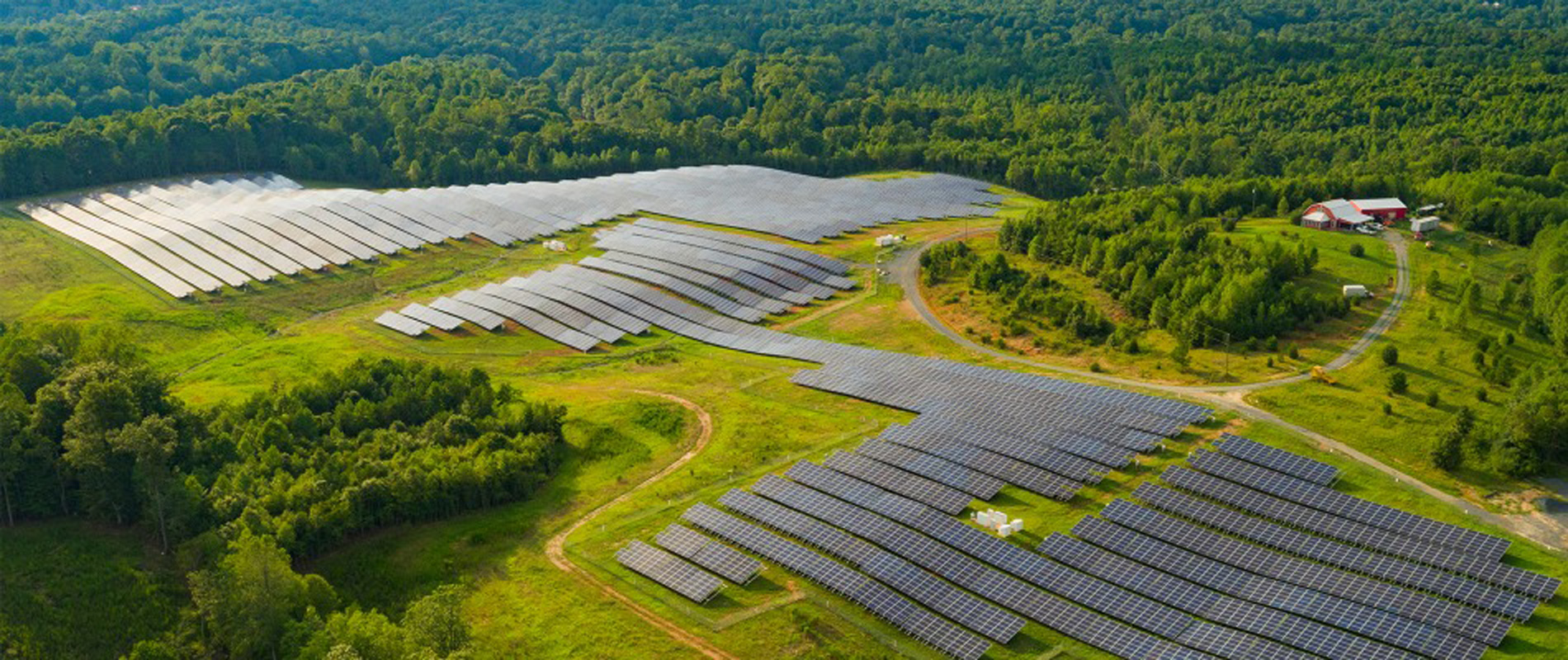 Aerial view of a solar farm with trees and a red farm house.