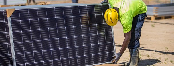 Construction worker in hard hat picking up solar panel on a site
