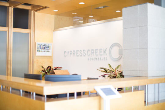 A large welcome desk of an office building with a sign reading Cypress Creek Renewables in the background