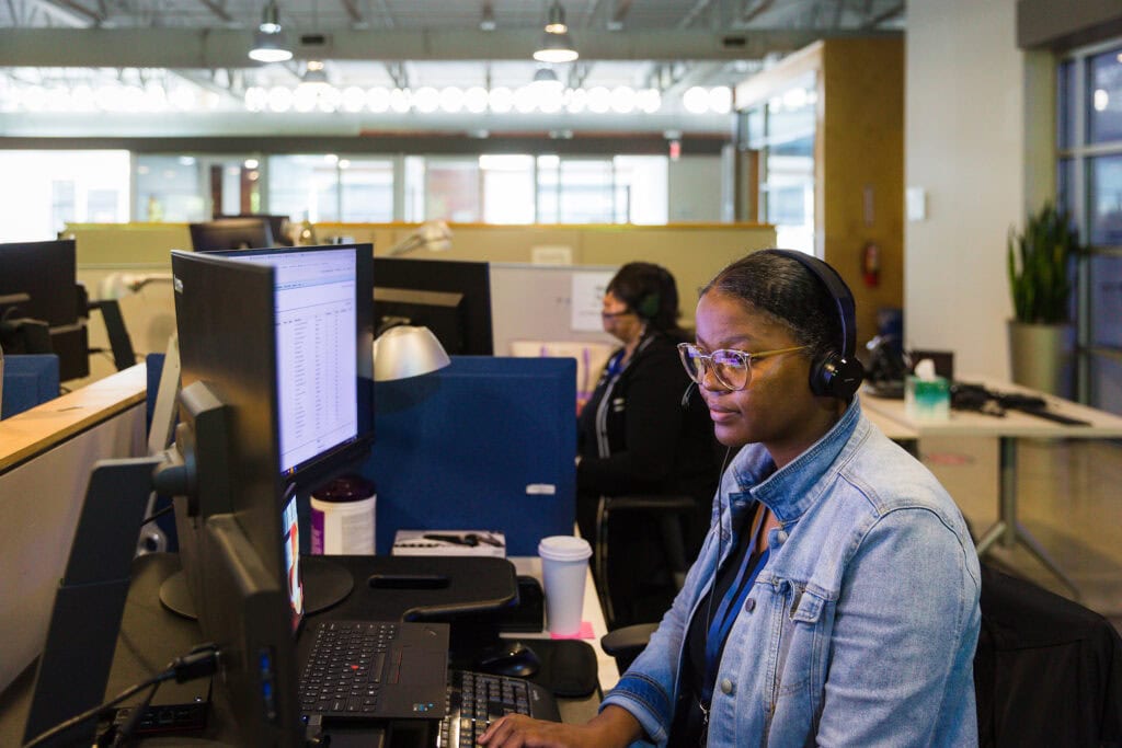 A woman wearing a headset sits at a computer in an office