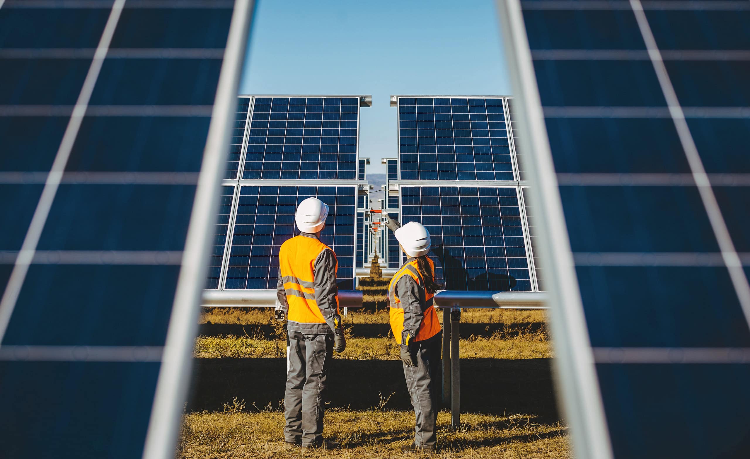 A man and a woman in safety gear look at and point at solar panels