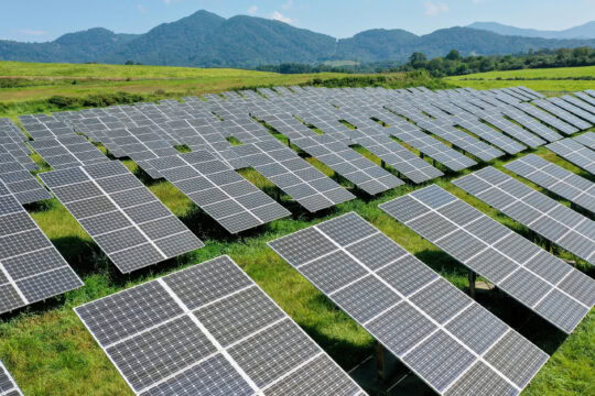 Solar panels are seen in rows with a mountain in the background