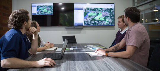 Employees in a conference room looking at research on the large screens that are showing zoning infomation