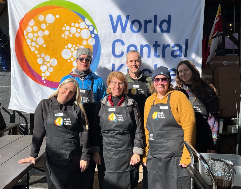 A group of size people wearing aprons pose in front of a banner reading "World Central Kitchen"