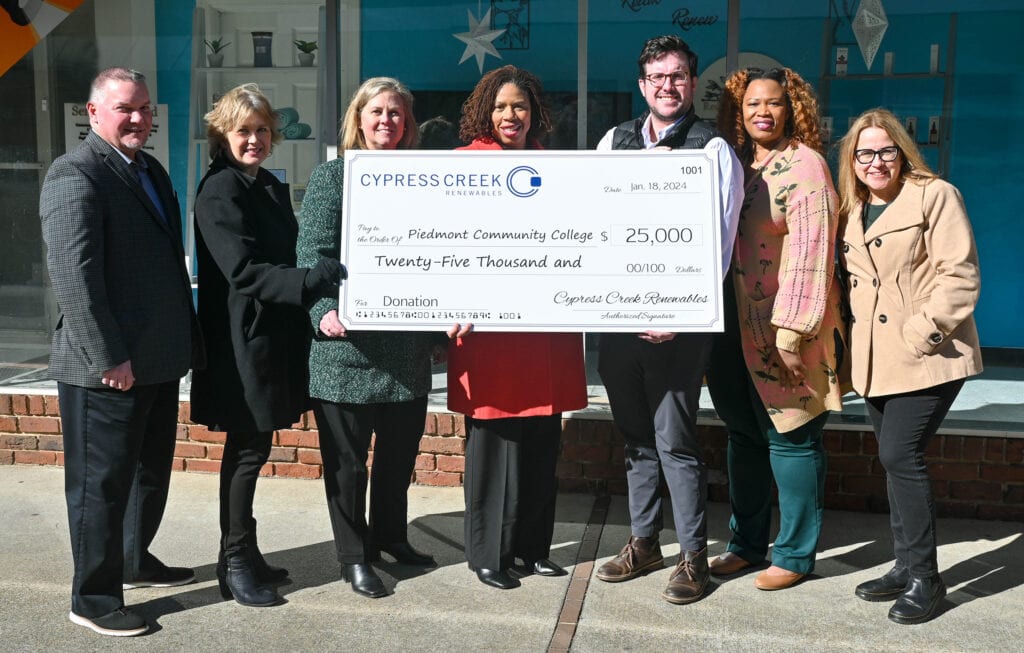 A group of seven people stand in a line holding a large check