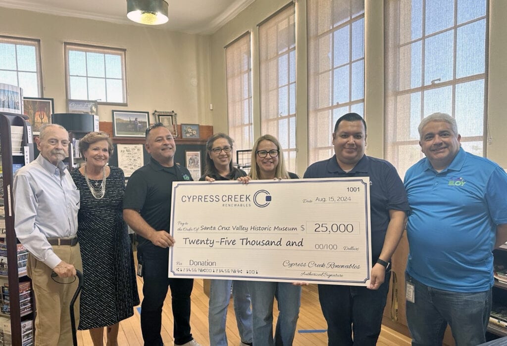 A group of seven people hold a large check addressed to the Santa Cruz Valley Historic Museum for $25,000 inside of a museum gift shop.