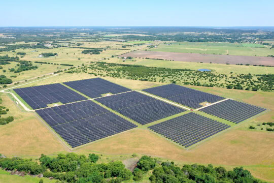 A solar farm is seen from above on a flat landscape