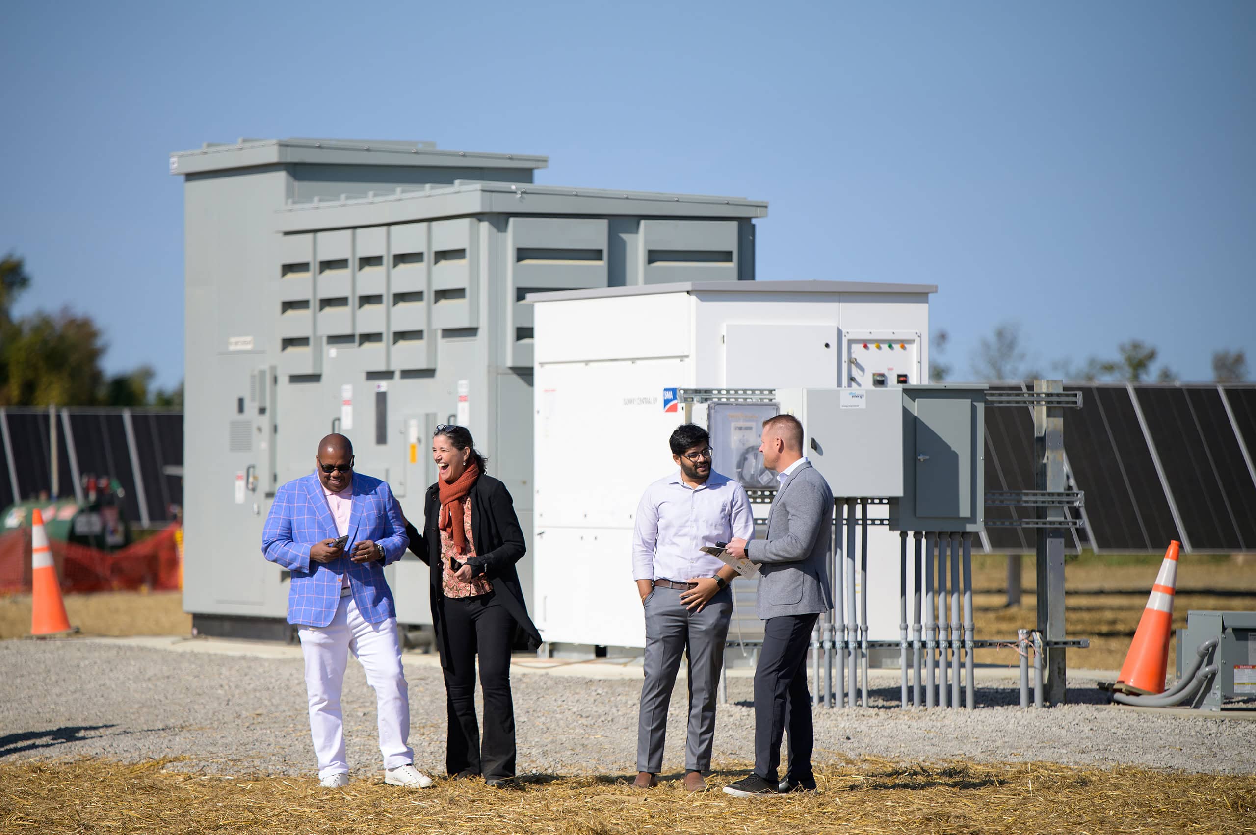 A group of four people stand in front of a transformer on a solar site talking and laughing