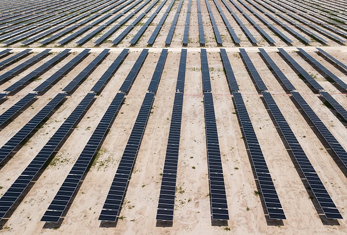 A solar farm is seen from above with multiple rows of panels stretching vertically across the frame.