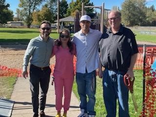 Three men and one woman pose in a line in a park