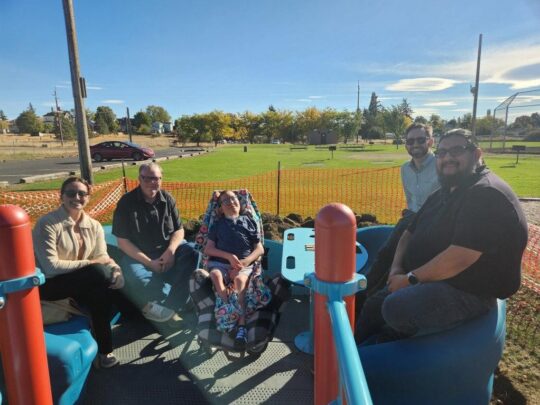 A group of people with a child in a wheelchair pose surrounded by playground equipment