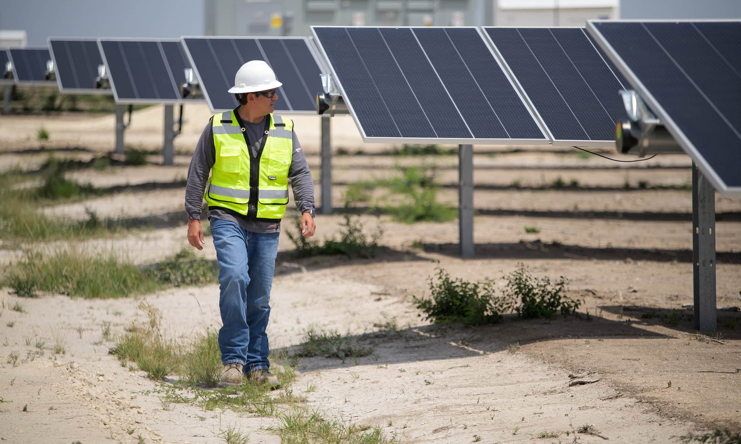 A man is safety gear walks past rows of solar panels